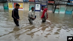 পাকিস্তানের লাহোরে বর্ষার ভারী বৃষ্টির কারণে সৃষ্ট বন্যাপ্লাবিত এলাকার মধ্যে দিয়ে মানুষ হেঁটে যাচ্ছে। ৫ জুলাই, ২০২৩। 