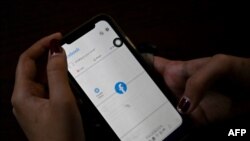 一名妇女使用手机在仰光查看Facebook，缅甸将军在夺权数天后下令互联网提供商限制访问Facebook。（2021年2月4日） （STR /法新社） 