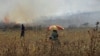 A Palestinian protester sits as a burning farm is seen during clashes with Israeli troops following the killing of an 18-month-old Palestinian toddler, at the Israeli Hawara checkpoint near the West Bank city of Nablus, July 31, 2015.