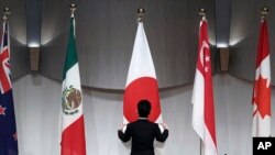  一名工作人员在东京举行的由日本主导的《跨太平洋伙伴全面进步协定》会议举行联合记者会前整理会场旗帜。（2019年1月19日） 一名工作人员在东京举行的由日本主导的《跨太平洋伙伴全面进步协定》会议举行联合记者会前整理会场旗帜。（2019年1月19日