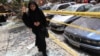 A woman walks over shattered glass, past damaged cars near the site of an explosion in Beirut's southern suburbs, Jul. 9, 2013.