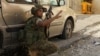 A Lebanese army soldier takes a position behind a car near the mosque complex (background), where hardline Sunni cleric Sheikh Ahmed al-Assir was believed to be sheltering with his supporters in Abra near Sidon, southern Lebanon, June 24, 2013.