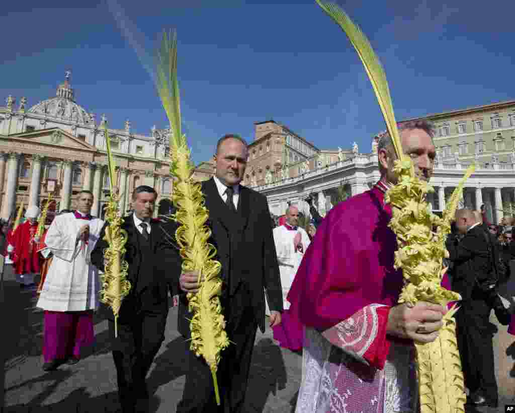 Prefect of the Papal Household Monsignor Georg Gaenswein, right, holds a palm leaf as he walks in procession at the beginning of a Palm Sunday Mass celebrated by Pope Francis, in St. Peter's Square, at the Vatican.