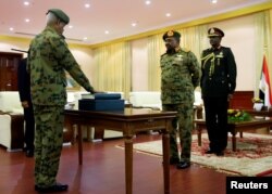 2019年2月24日，在苏丹总统解散政府后，国防部长伊本·奥夫（左）在总统巴希尔面前宣誓就任第一副总统。